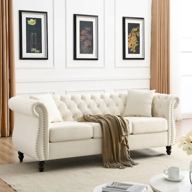 Beige velvet three-seater sofa with rolled-up armrests and rivet decorations; seats 3 people.