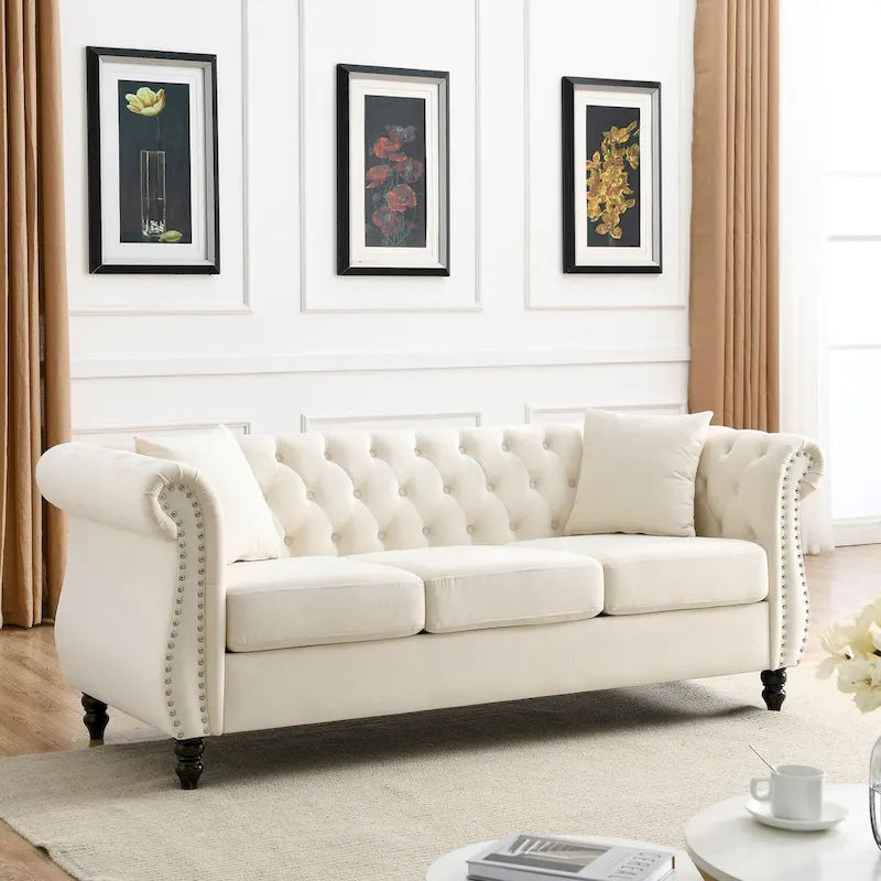 Beige velvet three-seater sofa with rolled-up armrests and rivet decorations; seats 3 people.