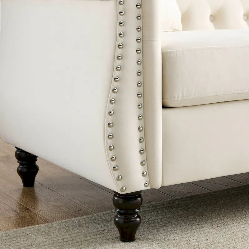 Beige velvet three-seater sofa with rolled-up armrests and rivet decorations; seats 3 people.