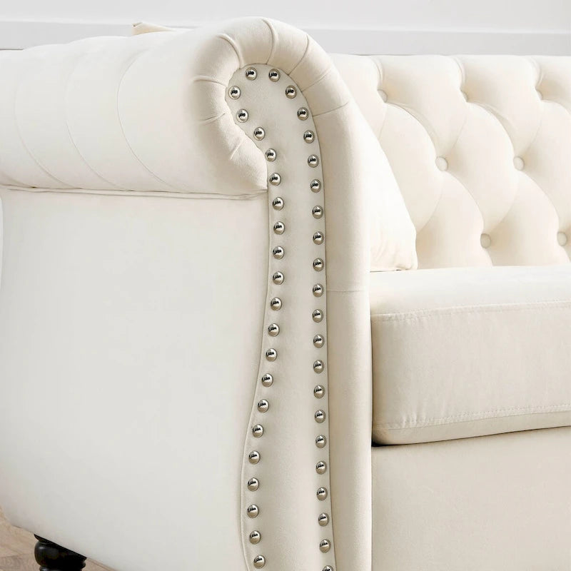 Beige velvet three-seater sofa with rolled-up armrests and rivet decorations; seats 3 people.