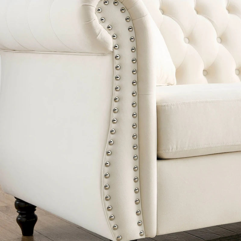 Beige velvet three-seater sofa with rolled-up armrests and rivet decorations; seats 3 people.