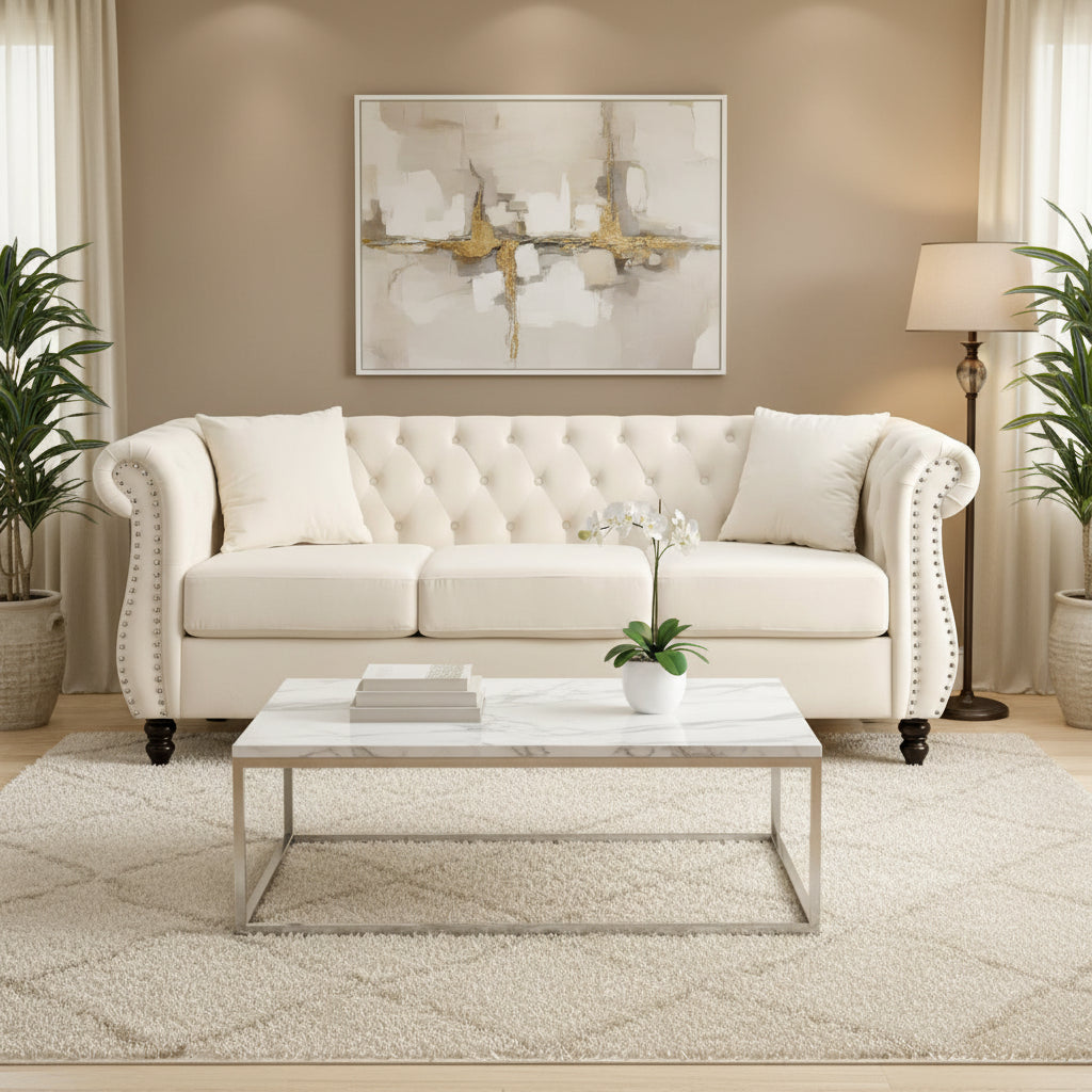 Beige velvet three-seater sofa with rolled-up armrests and rivet decorations; seats 3 people.